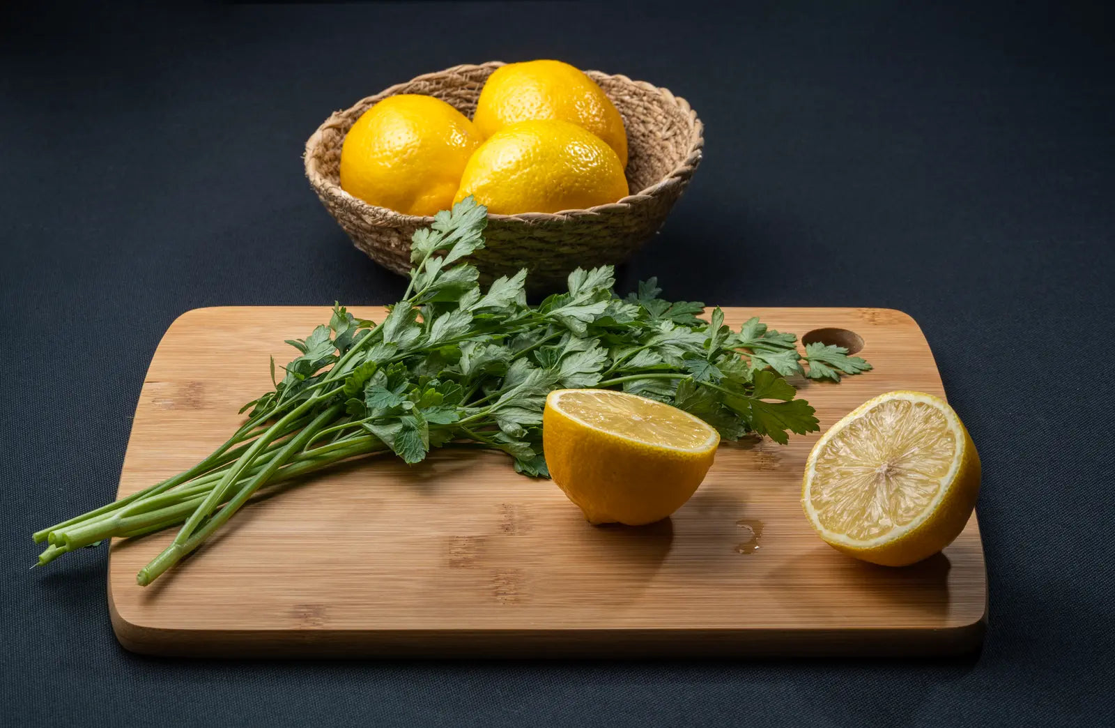 Fresh flat-leaf parsley and citrus zest on a wooden board next to small bowls of ground spice