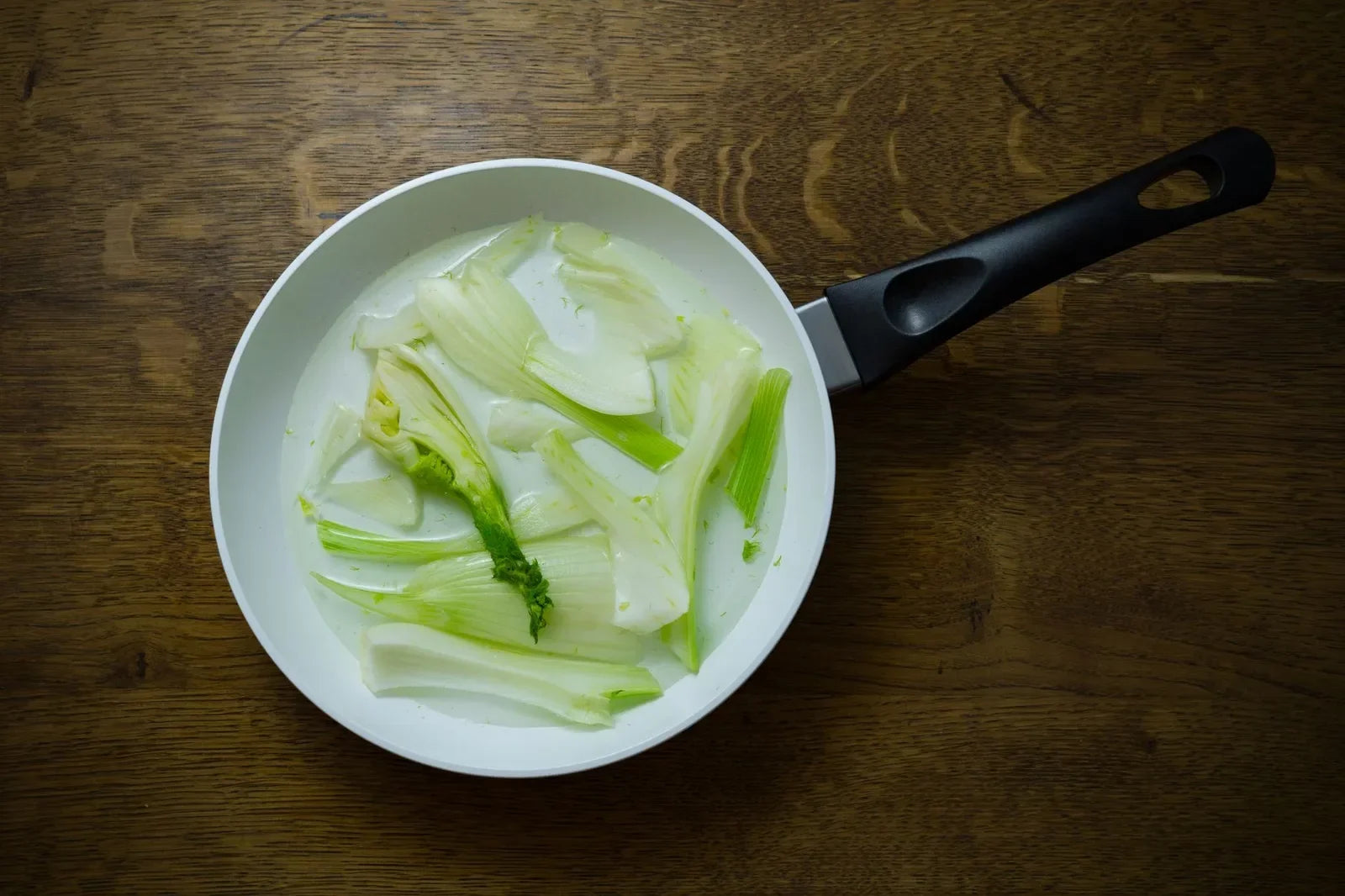 A sliced fennel bulb with feathery fronds and fresh tarragon on a wooden board