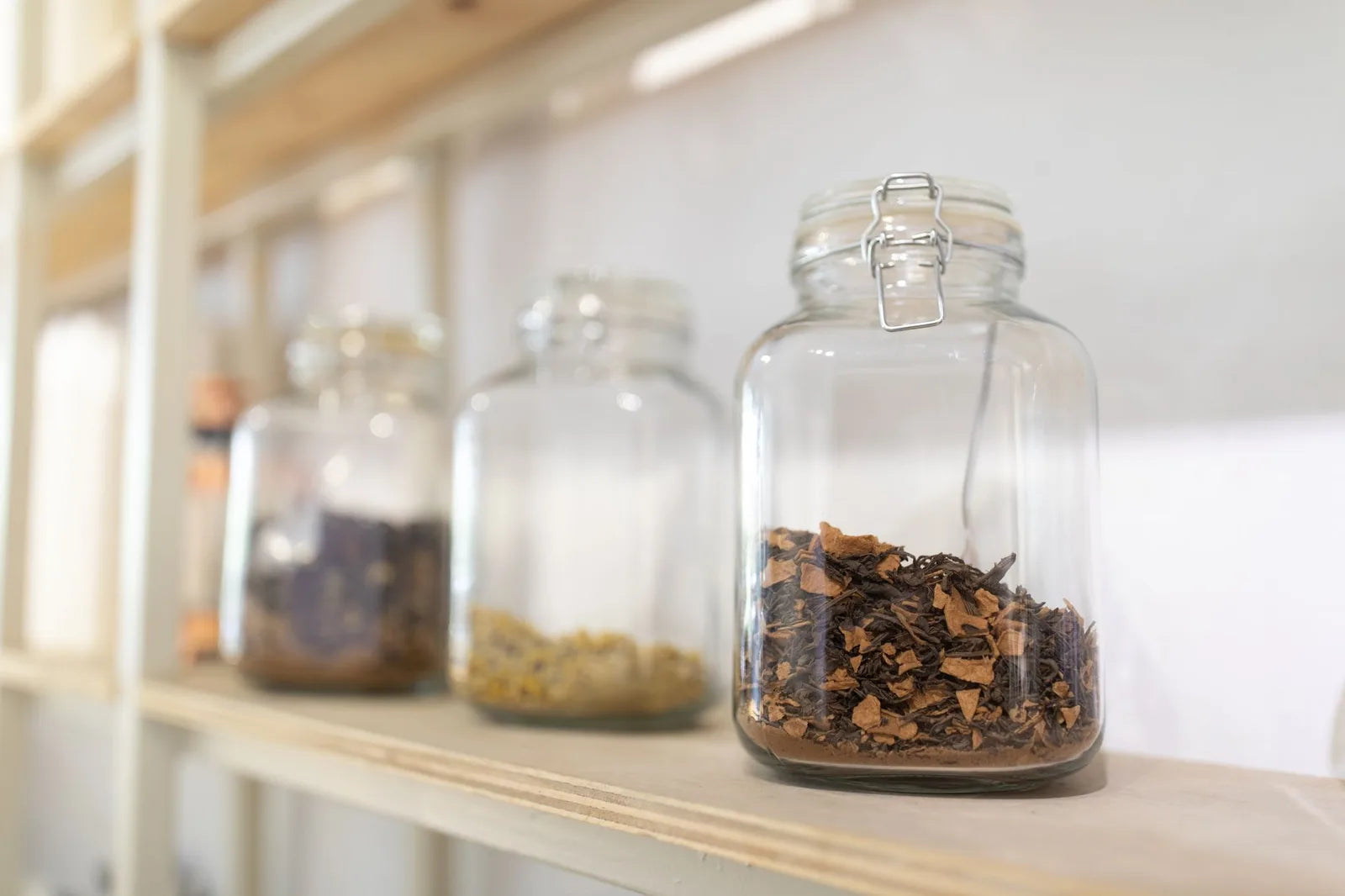 Glass jars of dried herbs and ground spices on a wooden counter